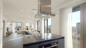 A modern kitchen with a central island, a dining area with a sofa and chairs, and large windows offering city views. - Capital Stay - Three Bed Apartment In Excel (London)