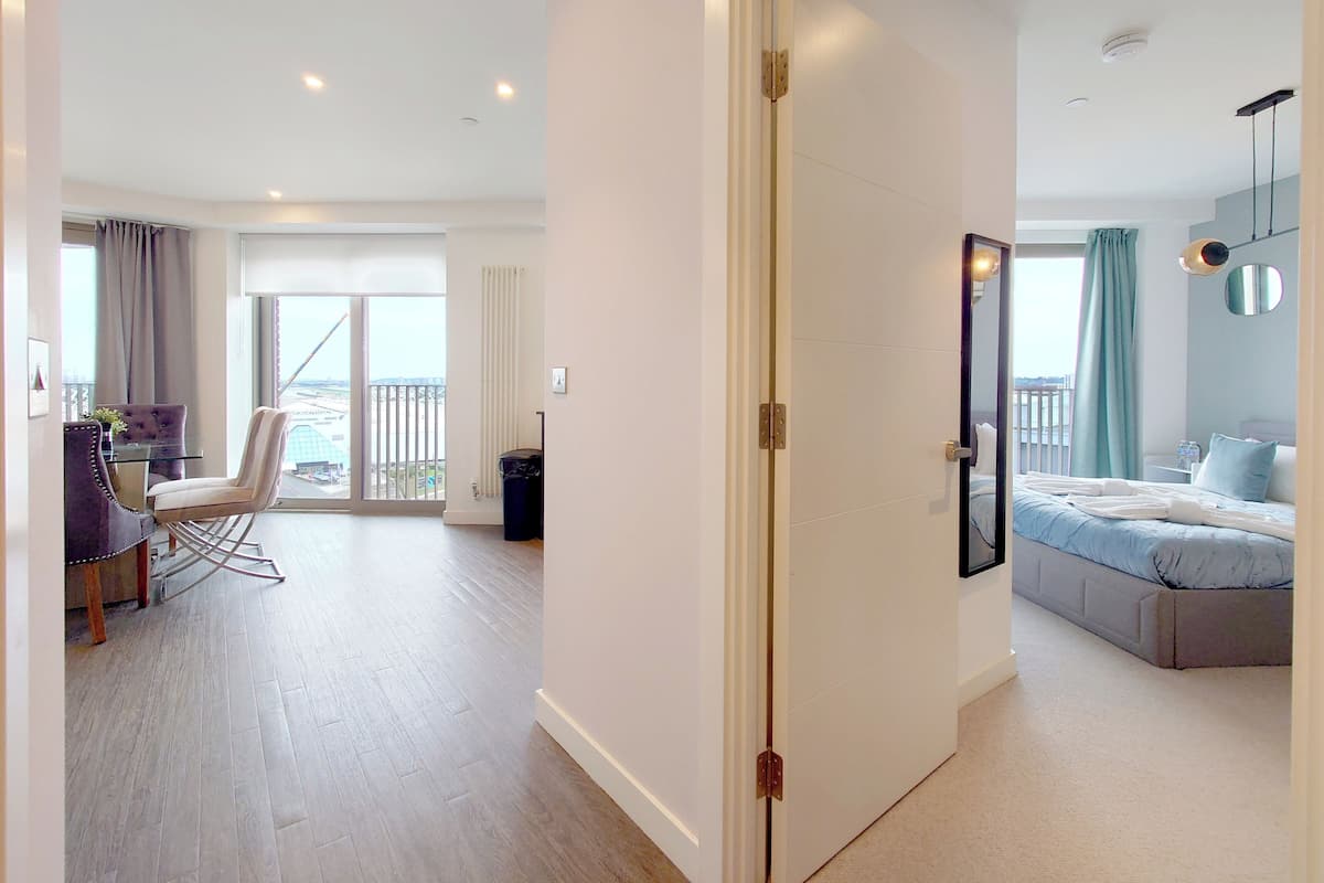 A modern apartment with a balcony, a dining area with a chair and table, and a bedroom with a bed and a nightstand.