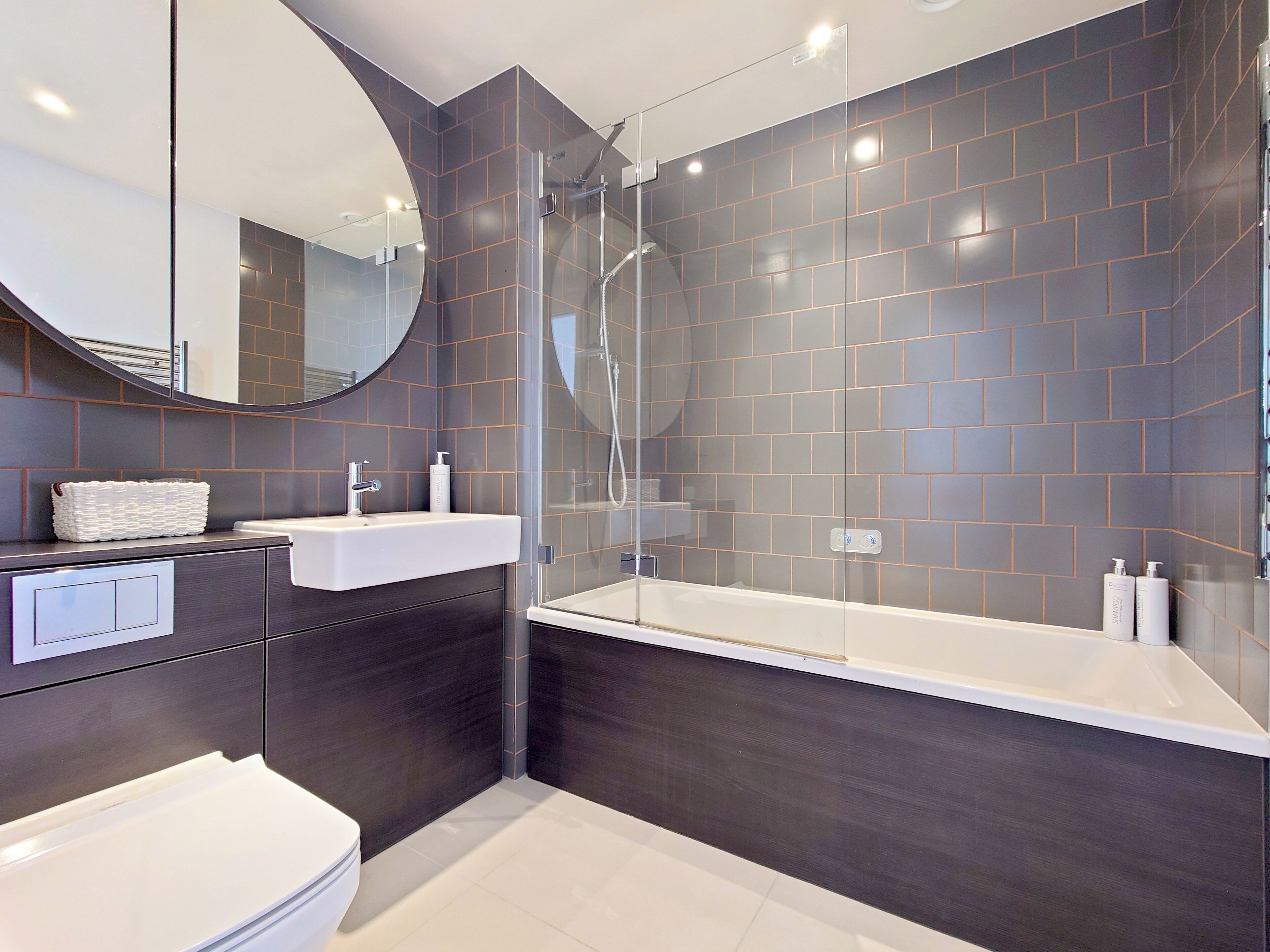 A modern bathroom with a glass-enclosed shower, a white sink, and a dark tiled wall.