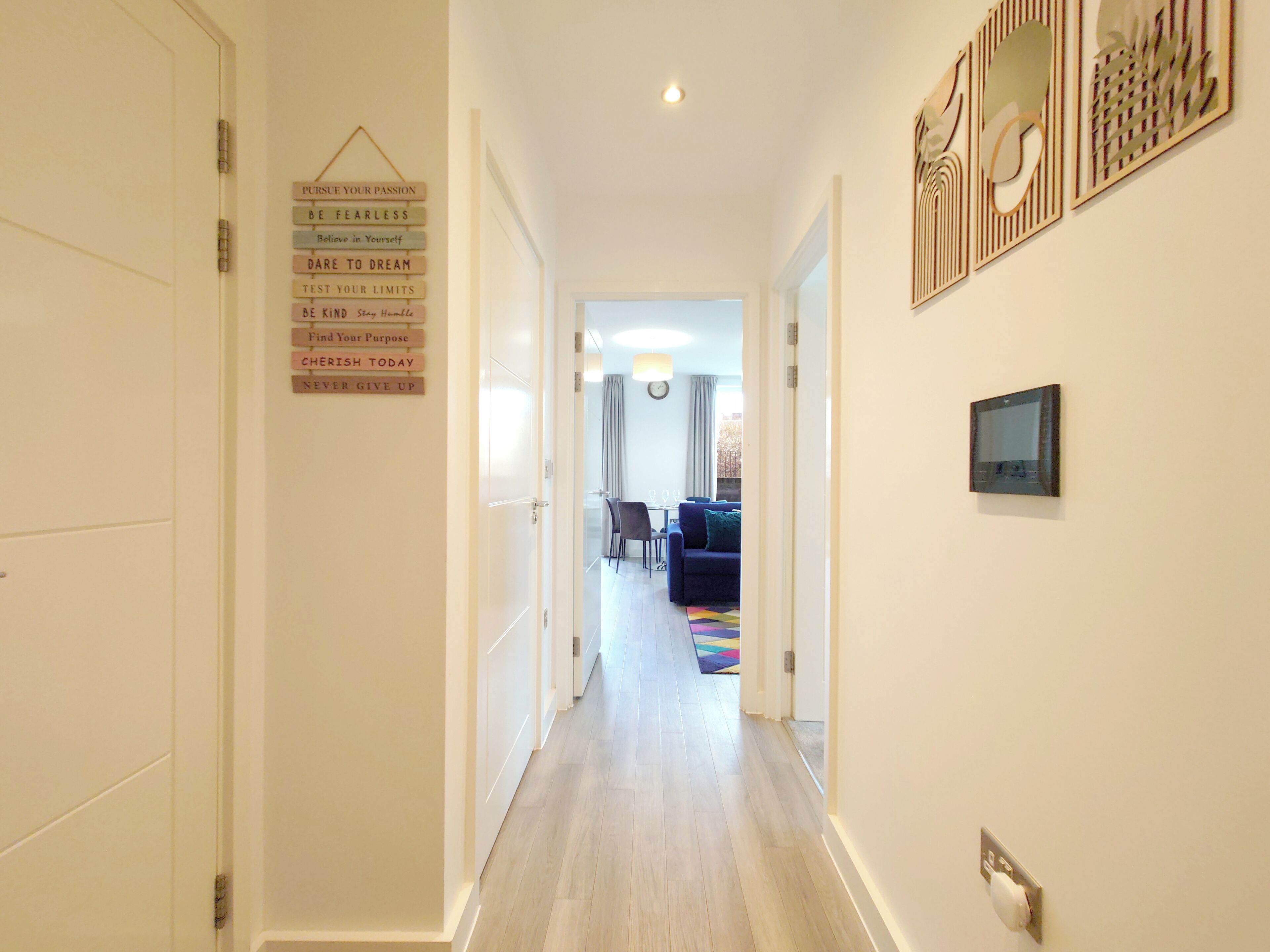 A hallway with a motivational poster, a dining area with a table and chairs, and a living room with a sofa and a TV.