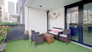 A balcony with wicker furniture, a sofa, and a glass door leading to a kitchen. - Luxury One Bed Apartment Near Olympic Park (London)