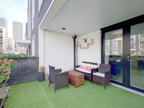 Ein Balkon mit Korbmöbeln, einer Couch und einer Glastür zu einer Küche.