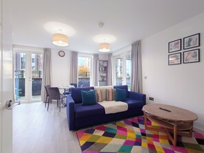 Ein Wohnzimmer mit Sofa, Couchtisch, Esstisch mit Stühlen und einem Balkon mit Vorhängen.