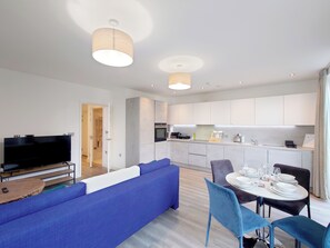 Ein modernes Wohnzimmer mit Flachbildfernseher, einem blauen Sofa und einem Essbereich mit Tisch für vier Personen.