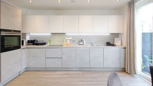 A modern kitchen with built-in appliances, a large window, and a view of greenery outside. - Luxury One Bed Apartment Near Olympic Park (London)
