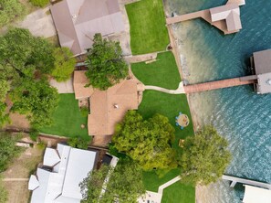 An aerial view of a residential property with a swimming pool, a wooden deck, and a grassy lawn. - Cedar Creek Lake Escape • Lakefront + Private Dock (Mabank)