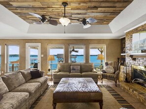 A spacious living room with a large window overlooking a body of water, a fireplace, and a ceiling fan. - Cedar Creek Lake Escape • Lakefront + Private Dock (Mabank)
