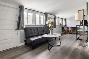 Ein modernes Wohnzimmer mit einer schwarzen Ledersofa, einem runden Couchtisch, einer Topfpflanze mit Orchideen und einem Essbereich mit zwei Stühlen und einem Tisch.