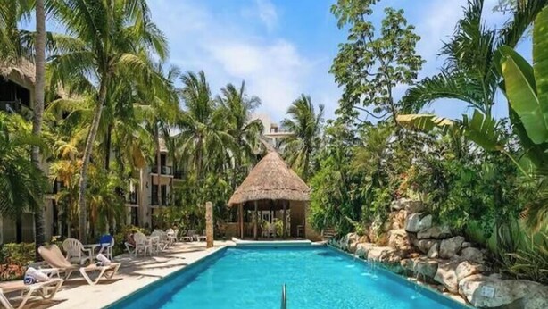 Ein Swimmingpool mit Liegestühlen und einer strohgedeckten Struktur, umgeben von Palmen.
