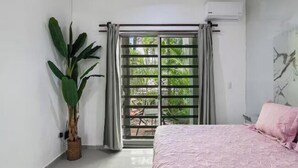 Ein Schlafzimmer mit einem Bett, einer Topfpflanze, einem Fenster mit Vorhängen und einer Klimaanlage.