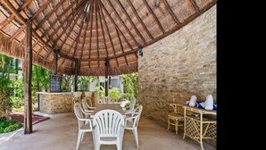 Eine Terrasse im Freien mit einem Reetdach, weißen Korbstühlen und einer Steinmauer.