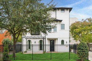 A two-story white building with a black door and windows, surrounded by a black fence and a green lawn. - Elegant Home With Elevator @Med Center, MDAnderson, NRG, Rice University (Houston)