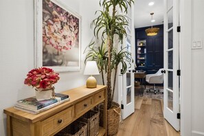 A hallway with a wooden console table, a potted plant, a lamp, and a framed floral artwork. - Elegant Home With Elevator @Med Center, MDAnderson, NRG, Rice University (Houston)