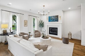 A modern living room with a white sofa, a round coffee table, a fireplace, and a chandelier. - Elegant Home With Elevator @Med Center, MDAnderson, NRG, Rice University (Houston)