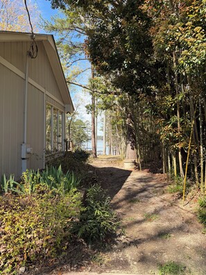 A pathway leading to a building with a sloped roof and large windows, surrounded by dense foliage and bamboo trees. - Spacious 4-bedroom lake house in delightful Manson with AC/ rec room/ dock (Manson)