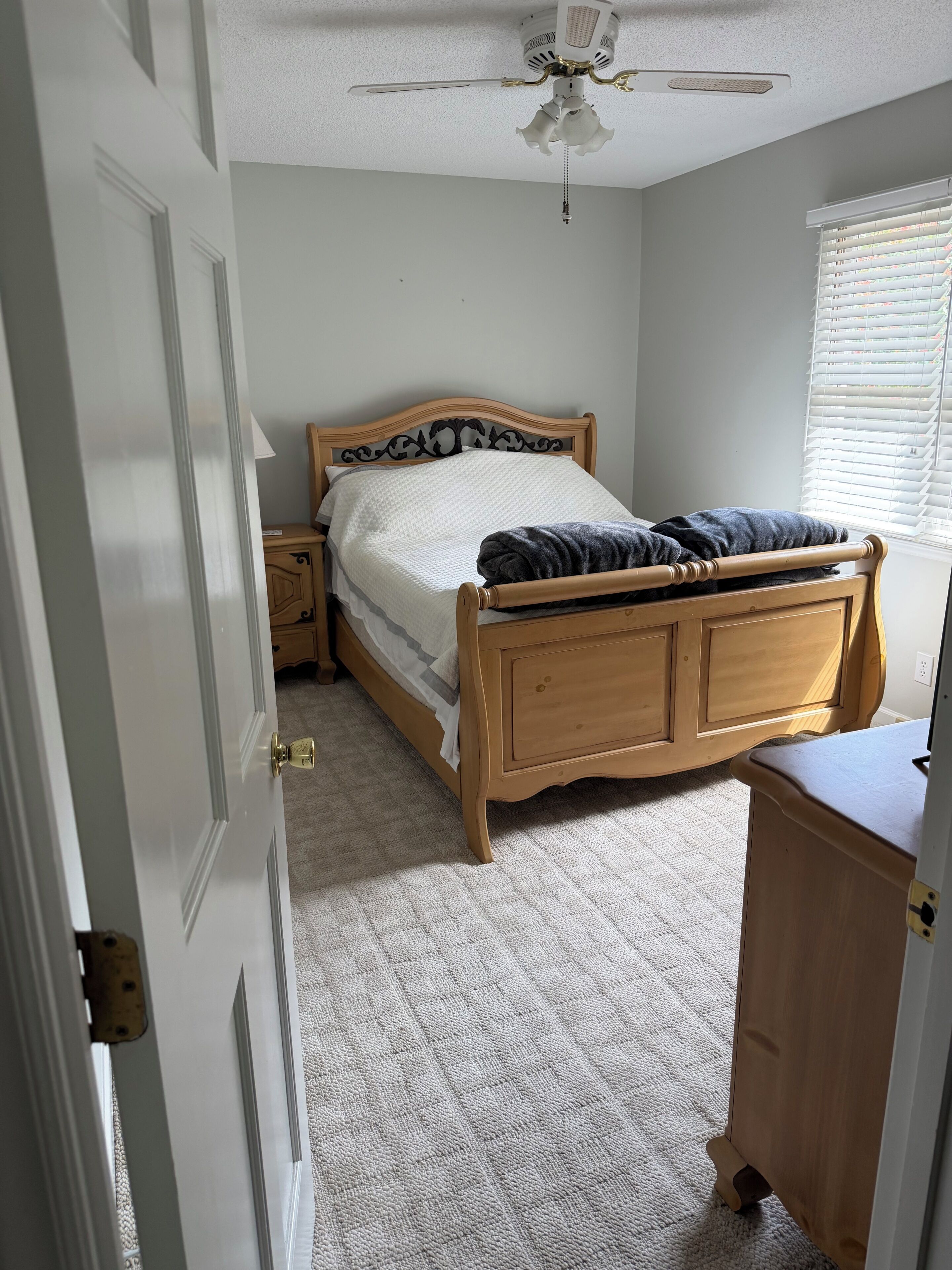A bedroom with a wooden bed, a nightstand, a ceiling fan, and a window with blinds.