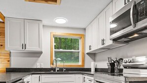 Una cocina moderna con armarios blancos, horno empotrado y ventana con vista a follaje.