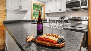 Una cocina con armarios blancos, encimera de madera, una botella de vino, dos copas y una tabla de embutidos.