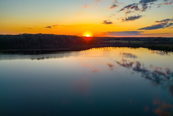Un lago tranquilo que refleja el atardecer, con un bosque al fondo.