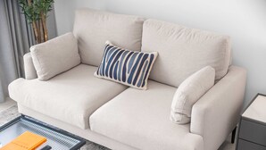 A beige sofa with a striped pillow, a small side table, and a glass coffee table with a book and remote control. - Free Housekeeping Visits During Your Stay - Stayshort - Comfortable Studio Stay in Arjan Sleeps 2 With Balcony (Dubai)