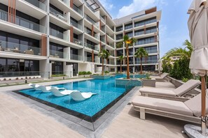 Un hôtel moderne doté d’une piscine, de chaises longues et de palmiers.