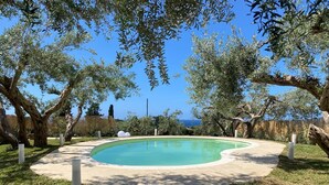 A swimming pool with a curved edge, surrounded by grass and trees, with a clear view of the sky and distant landscape. - Villa with Private Pool, Sea View in Sicily, Palermo-Terrasini. Family friendly (Serra)