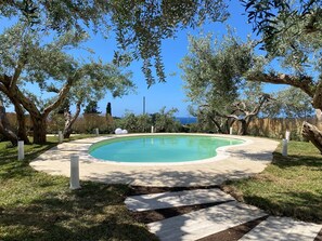 A swimming pool with a curved edge, surrounded by grass and trees, with a clear view of the sky and distant landscape. - Villa with Private Pool, Sea View in Sicily, Palermo-Terrasini. Family friendly (Serra)