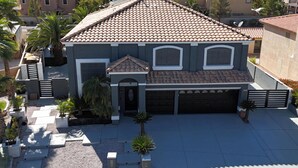 A residential building with a tiled roof, a garage, and a landscaped front yard with palm trees and planters. - Luxurious 6-Bedroom House In Las Vegas with Pool And Spa - EV Charger (Las Vegas)