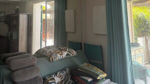 Een kamer met een bed, een raam met gordijnen, een airconditioningapparaat, een lijst met een foto aan de muur, en een spiegel.