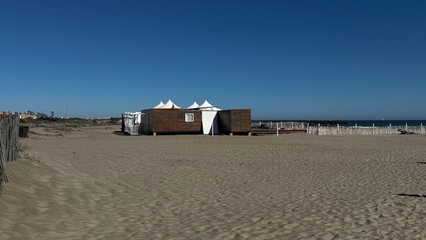 Een zandstrand met een houten constructie, in de verte staat daar 'JAMBOREE' op.