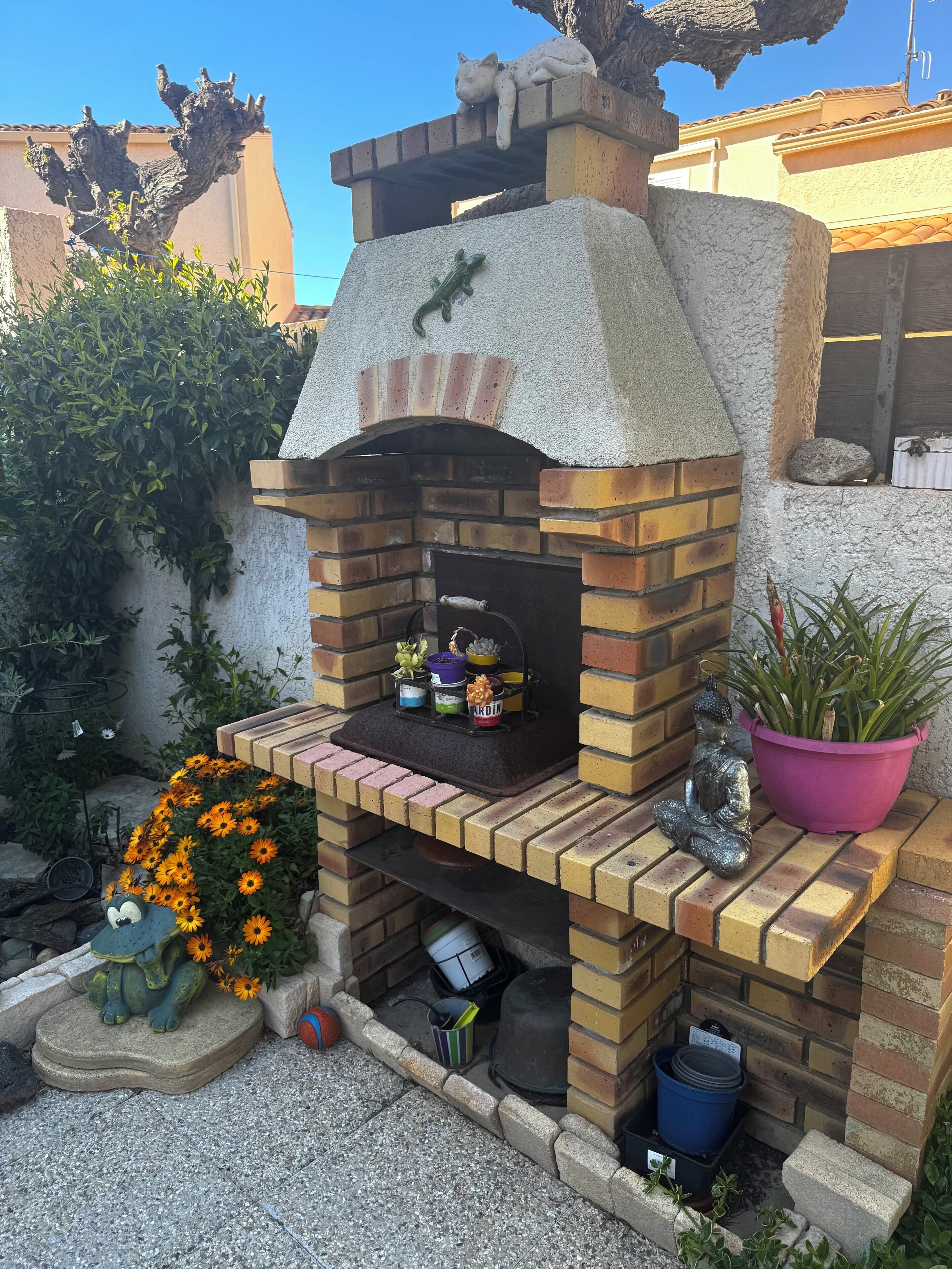 A brick outdoor oven with a rustic design, surrounded by potted plants and decorative items.