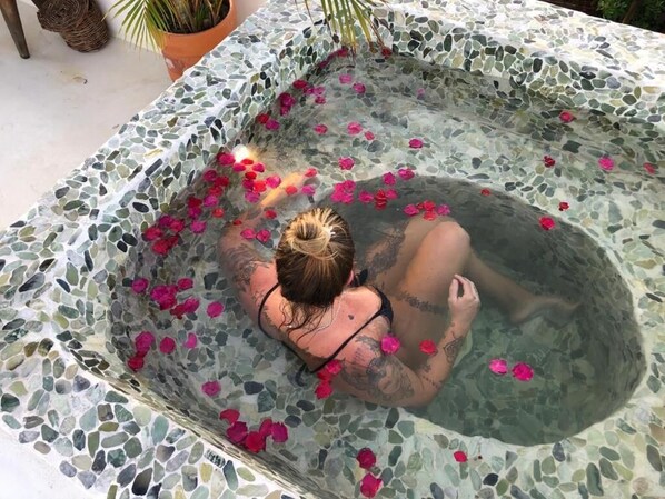 A person in a hot tub with mosaic tiles and pink flower petals. - Villa Fulô Casa Hotel (Porto Seguro)