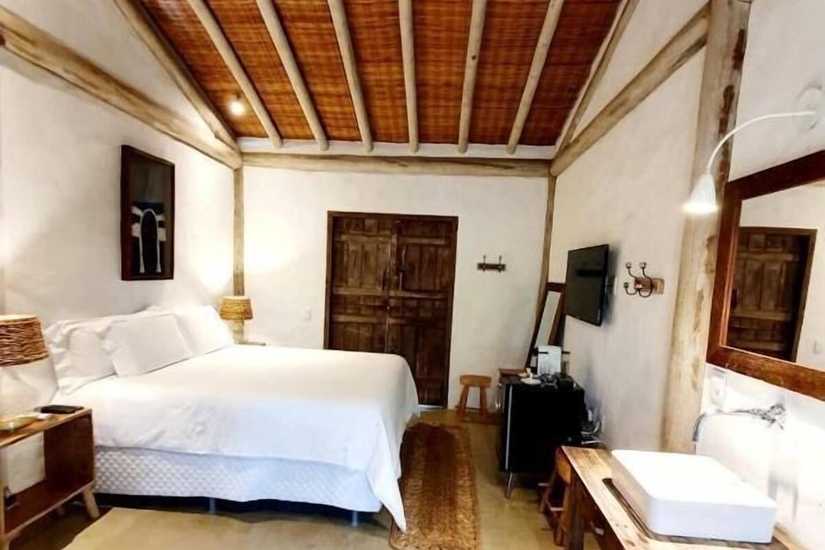 Un dormitorio con techo de madera, una cama, una mesita de noche, un aparador, un espejo y una ventana.