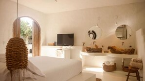 A bedroom with a bed, a TV, a large mirror, and a wooden shelf with towels. - Villa Fulô Casa Hotel (Porto Seguro)