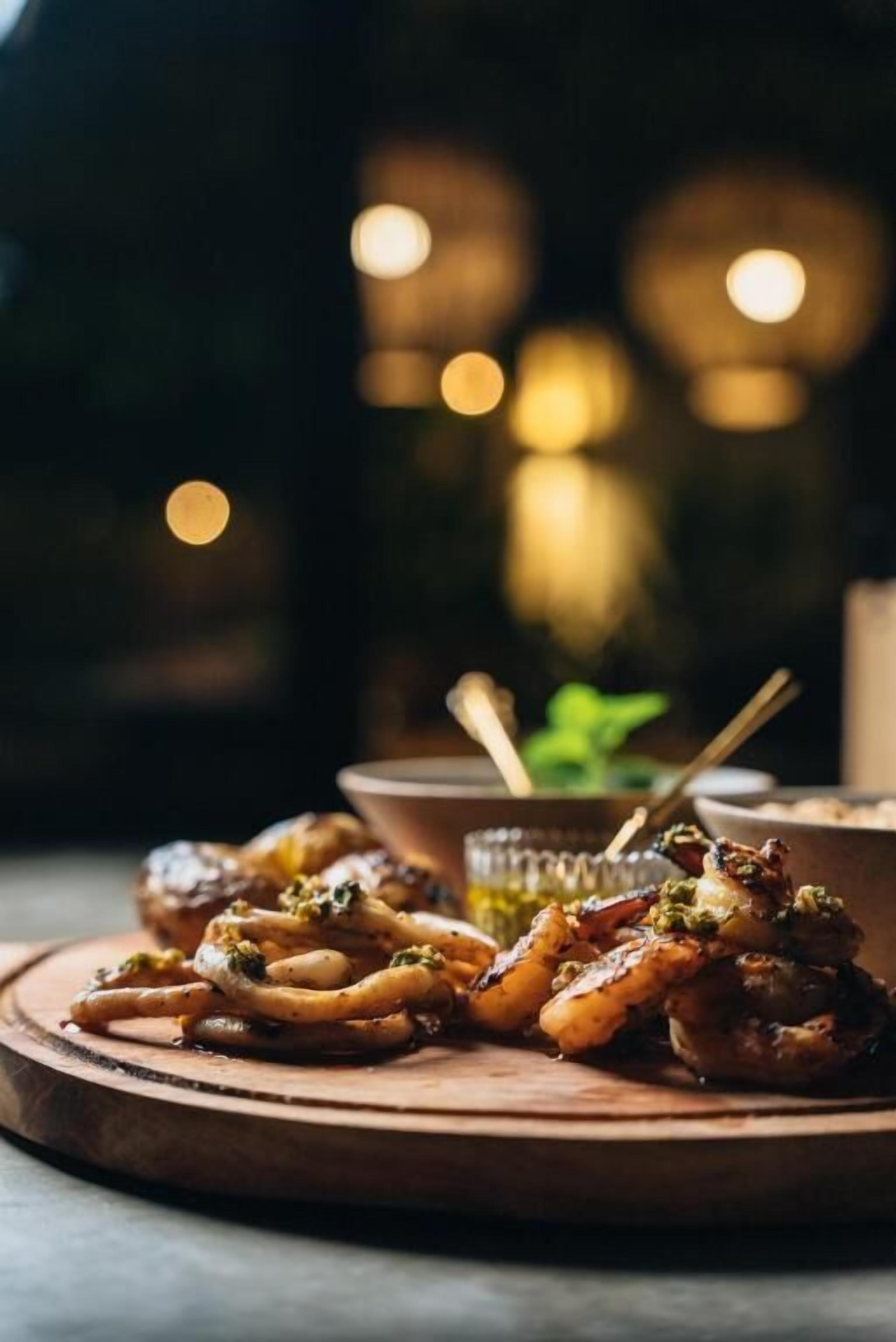 A wooden board with grilled food, a bowl, and a spoon.