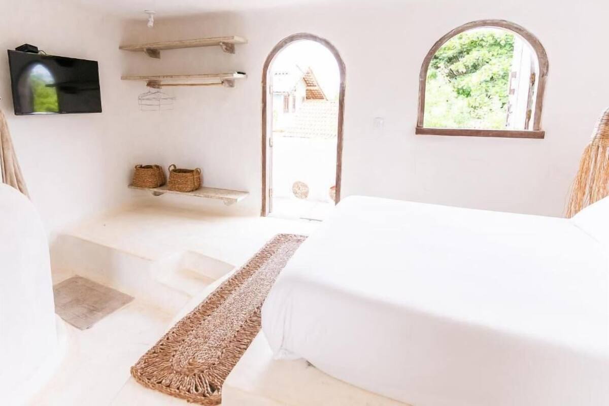 Un dormitorio con cama, televisor, ventana y un pequeño estante con cestas.