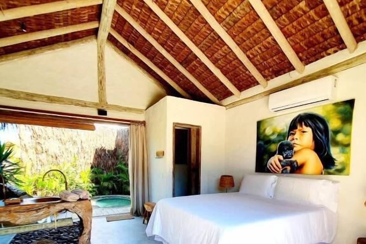 Un dormitorio con cama, un cuadro, una mesa de madera y vistas al verdor.