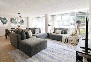 Ein modernes Wohnzimmer mit einer Eckcouch, einem Esstisch und einem großen Fenster mit Ausblick.