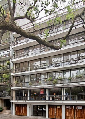 Ein mehrstöckiges Gebäude mit Balkonen, großen Fenstern und einem Baum im Vordergrund.