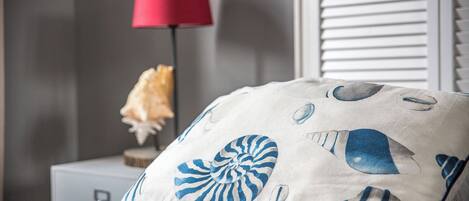 Een bed met een sierkussen met schelpmotieven, een rode lamp en een witte muur.