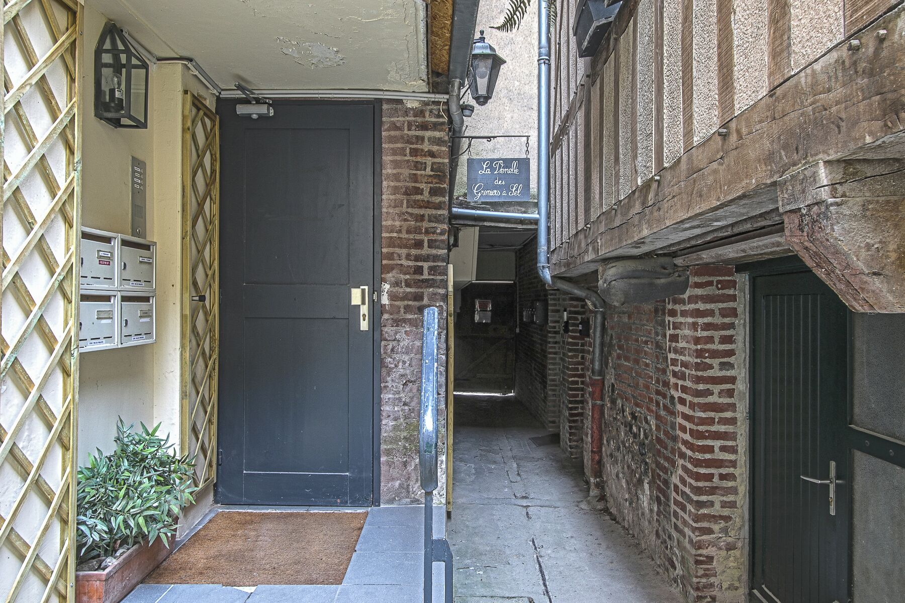 Un estrecho callejón con una puerta negra, una reja metálica y un edificio de ladrillo con un letrero sobre la puerta.