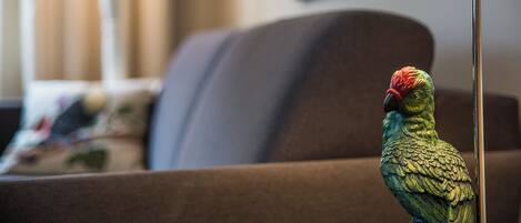 A parrot on a brown sofa with a lamp in the foreground.