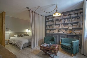 Une chambre à coucher avec un lit, un bureau, deux chaises, une bibliothèque et une valise.