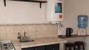 Eine Küche mit Gasherd, Spüle und Wasserspender. Zwei Hocker und ein Tisch mit Kerze stehen bereit.