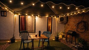 Eine Terrasse im Freien mit Tisch, Stühlen, Lichterketten, Blumentöpfen und einer Backsteinmauer.