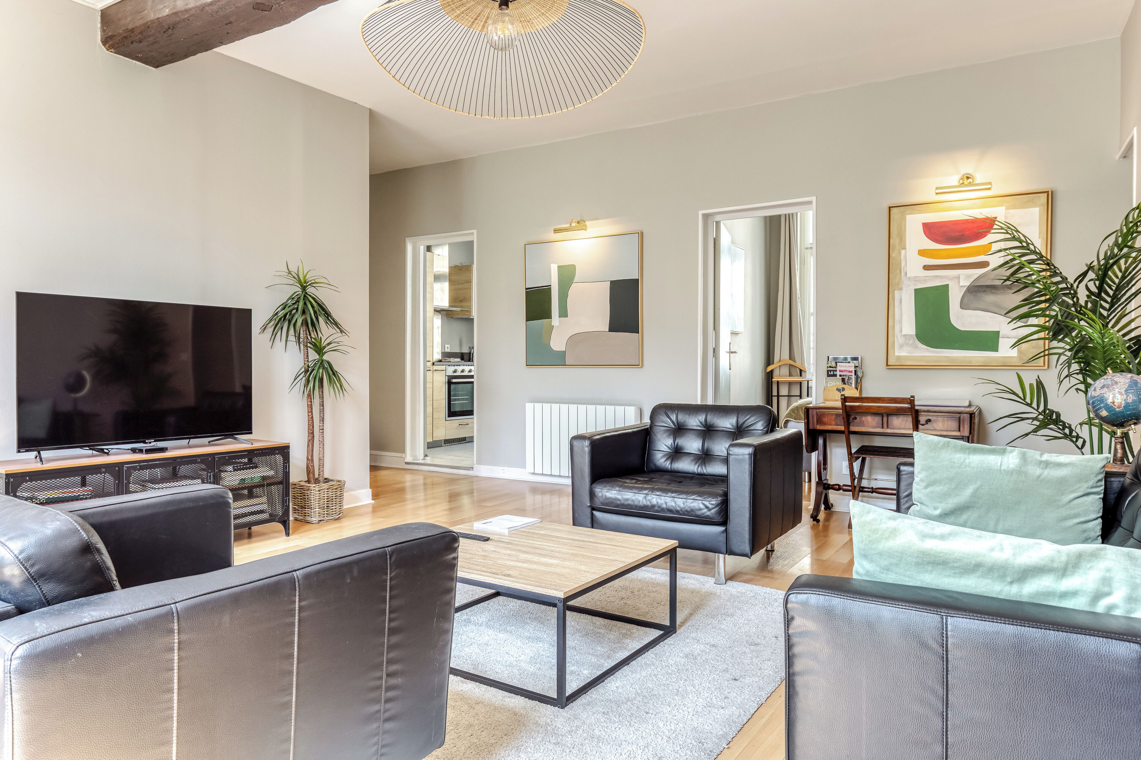 A modern living room with a flat-screen TV, leather sofas, a coffee table, and a dining area with a table and chairs.