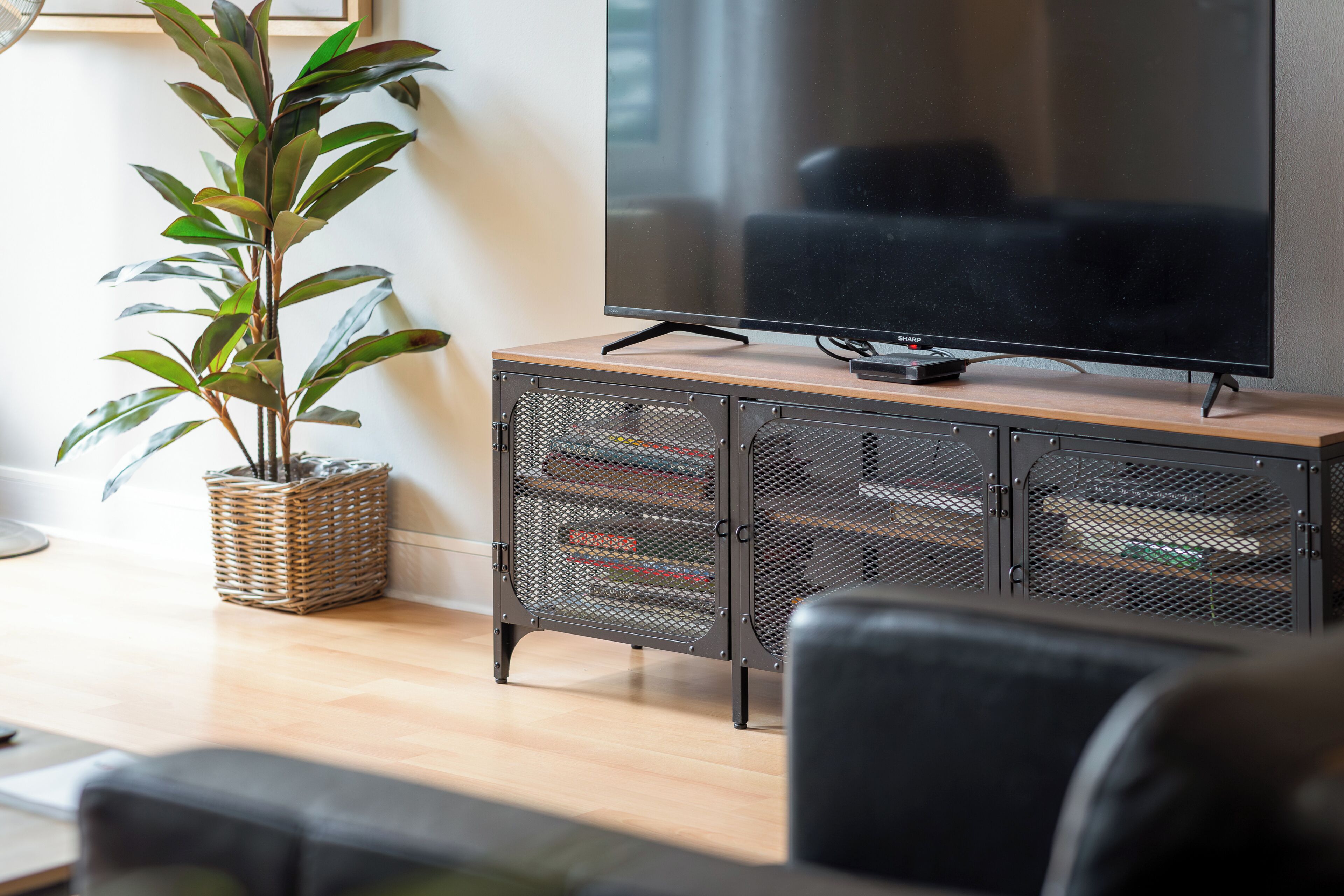Een woonkamer met een flatscreen televisie op een houten kast, een potplant en een leren bank.