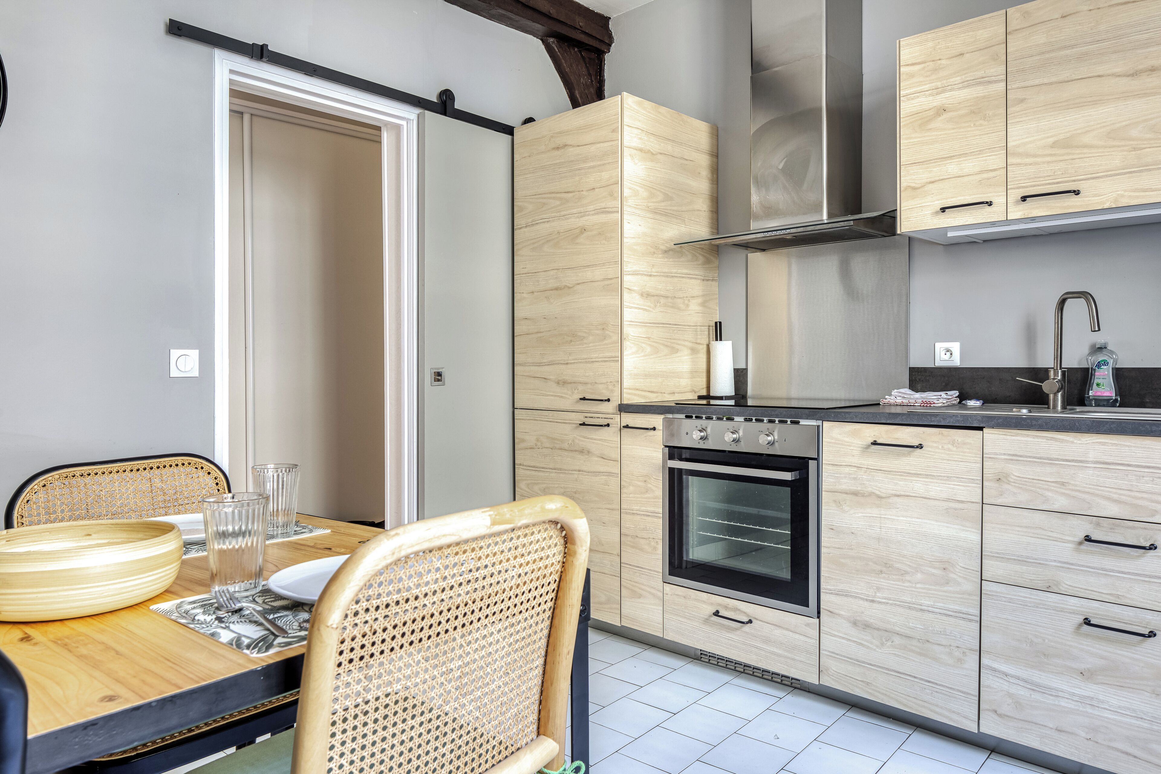 A modern kitchen with wooden cabinets, a stainless steel oven, and a dining area with a table and chairs.