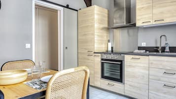 A modern kitchen with wooden cabinets, a stainless steel oven, and a dining area with a table and chairs.