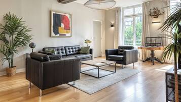 Un salon moderne comprenant un canapé, une table basse et des fauteuils, une table à manger décorée avec un motif de bateau, et une grande fenêtre avec des rideaux.